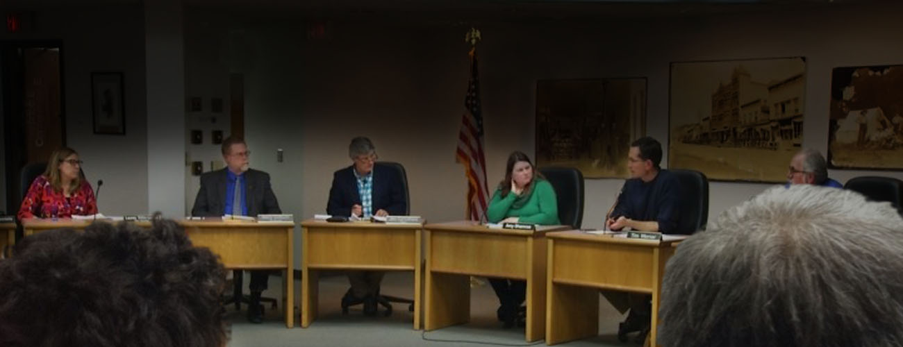 City Commission members sit at tables and discuss issues while an audience watches